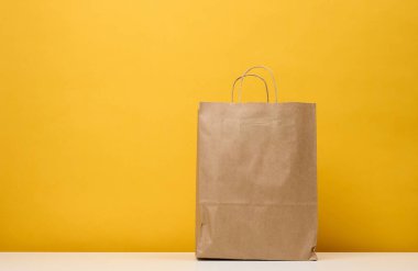 A brown paper bag stands on a white table, yellow background. Product packaging