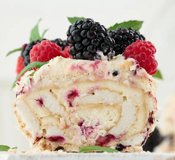 Baked meringue roll with cream and fresh fruits on a white wooden board, delicious dessert