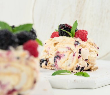 Baked meringue roll with cream and fresh fruits on a white wooden board, delicious dessert