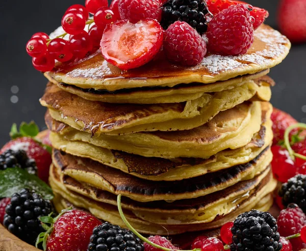 A stack of pancakes with fresh fruits poured with syrup on a black background