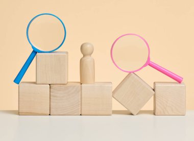 Tahta erkek figürleri bej bir arka plan ve mavi plastik büyüteç üzerinde dururlar. İşe alım konsepti, yetenekli ve yetenekli çalışanların aranması, kariyer gelişimi