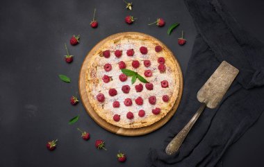 Round baked pie with apples and sprinkled with powdered sugar on a black table. View from above