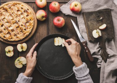 Bir kadın, elma dilimlerini masanın üzerine, malzemelerin yanına, yuvarlak bir yemek tepsisine koyar. Yukarıdan görüntüle