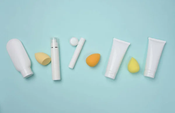 White plastic tubes for cream, gel and other cosmetics and sponges on a blue background, top view