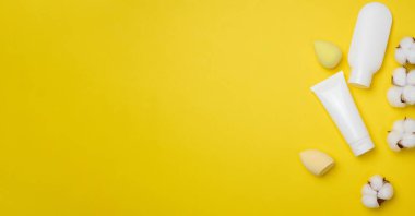 Beyaz plastik tüpler ve krem, jel ve diğer kozmetik ürünleri için kavanoz ve sarı arka planda süngerler, üst manzara. Boşluğu kopyala