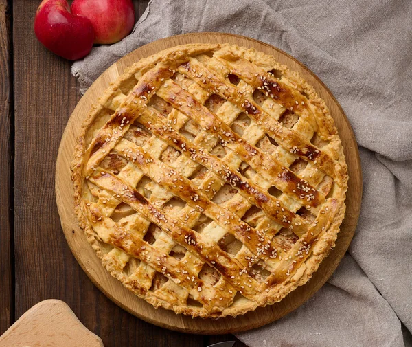 Round baked apple pie on a brown wooden table, top view