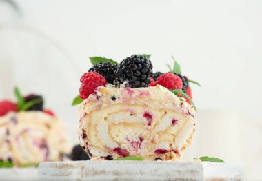 Baked meringue roll with cream and fresh fruits on a white wooden board, delicious dessert