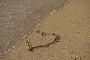 Bir dalga kuma çizilmiş bir kalbi alıp götürür.