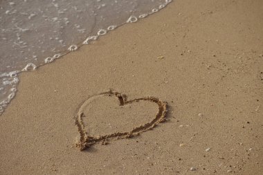 Bir dalga kuma çizilmiş bir kalbi alıp götürür.