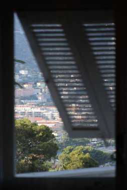 Denize bakan pencere. Ön plandaki kepenkler bulanık, deniz manzarası ve Fransız Riviera Sahili