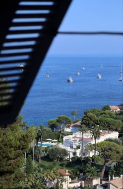 Denize bakan pencere. Ön plandaki kepenkler bulanık, deniz manzarası ve Fransız Riviera Sahili