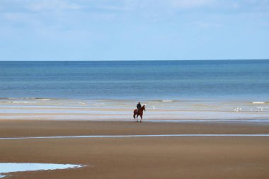 Adamın biri Cabourg sahilinde ata biniyor.