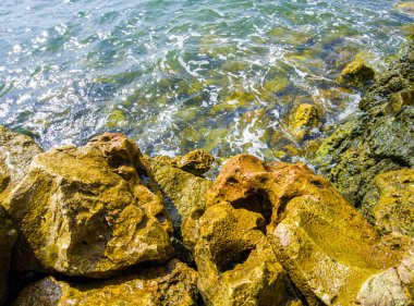 Kayalara vuran kumsal dalgaları, sahil manzaraları ve kayalar, kayaları ıslatan köpüklü su dalgaları.