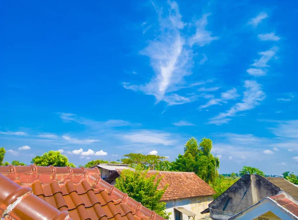 Several residential roofs in the village against the background of white clouds on a clear blue sky in the morning
