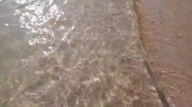 Küçük deniz suyu dalgaları kumsalda ileri geri hareket ediyor. Deniz dalgaları yaz tatilinde kumsalda yumuşak köpükle yavaşça hareket eder. 