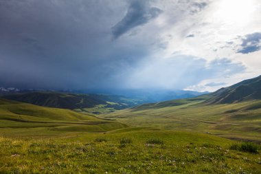 Endless pastures in the valley of the Assy plateau under thunderclouds with the sun, Asia, Kazakhstan