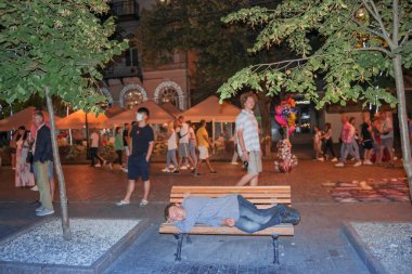 Odessa, Ukrayna - 15 Ağustos 2021: Evsiz bir adam parkta bir bankta uyuyor .