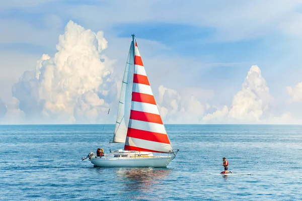 Beautiful clouds in the background. A boat with a red and white sail meets the surfer in the blue sea. Amazing concept design for outdoor recreation. Summer water sports, outdoor adventure
