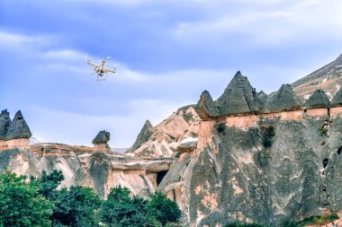 Çeyrek helikopter tepenin üzerinden uçuyor. Beyaz dron açık mavi gökyüzünde süzülüyor. Aero fotoğraf çekiminde yeni teknoloji. Kapadokya, Türkiye 'nin Orta Anadolu Bölgesi, Asya.
