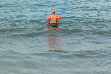 Yetişkin adam sudan korkar ama yüzmeyi öğrenmeye çalışır ve fırfırlarla denize açılır.
