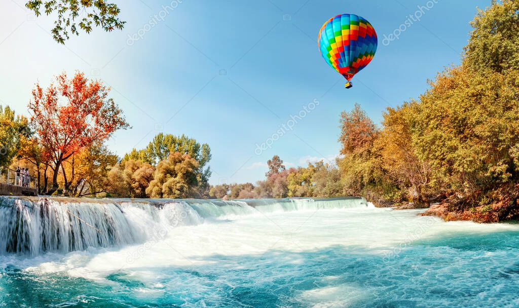 A beautiful multi-colored balloon flies over an autumn waterfall on the Manavgat River in Antalya, Turkey. Panoramic view.