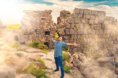 Ortaçağ harabelerinde güneşe doğru uzanan elleri olan bir adam. Arka planda gizemli sis var. Ayarlanmış