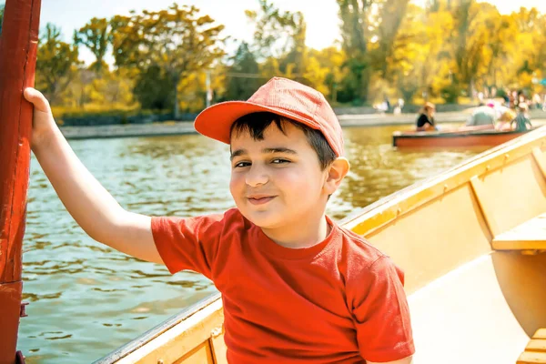 Happy boy in a red T-shirt and a baseball cap sails on a boat and holding an oar. Toned