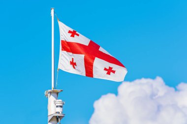 Gürcistan Bayrağı mavi arka planda bayrak direğinde sallanıyor.