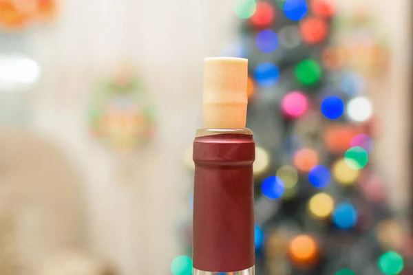 Open bottle of wine with a cork on the background of the defocused Christmas tree , festive background