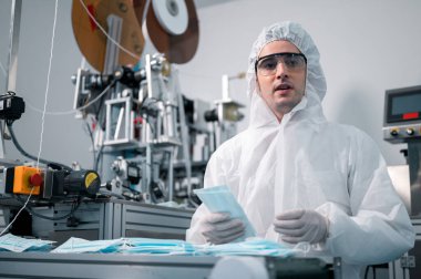 Bilim adamları üniforma giyiyorlar. Yüz maskelerinin üretim sürecini kontrol et. Sanayi tesislerindeki bir laboratuvarda. Güvenlik ve koruma konsepti Coronavirus covid-19.