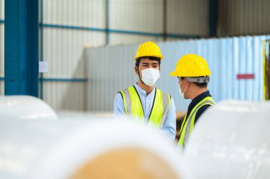 Mühendisler ve ustabaşı maske, şapka ve yelek giyerler. Endüstriyel üretim yönetimi hakkında görüşeceğim. İş detaylarını fabrikalarda veya depolarda dizüstü bilgisayarlar ve tabletler yoluyla açıklamak.