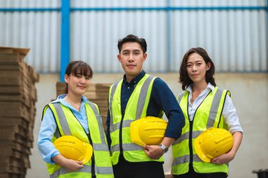 Fabrika çalışanı mühendislerden, ustabaşından ya da teknisyenlerden oluşur. Elinde bir kaskla yelek giyiyorsun. Sırada dur ve kameraya odaklan. Takım çalışması konsepti.