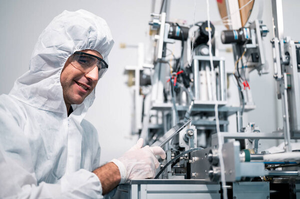 Scientists wearing protective clothing Inspect mask making machines in a laboratory at an industrial plant. Anti-virus production warehouse. concept of safety and prevention coronavirus covid-19.