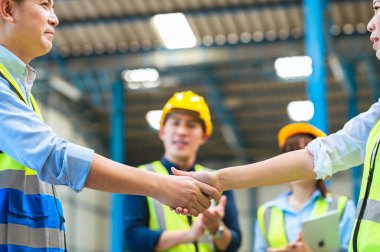 Mühendislerin, ustabaşının, teknisyenlerin ve personelin fabrika çalışanı. Maske, kasket ve yelek tak. Anlaşma yapmak için el sıkışın ya da organizasyonda ya da depoda başarıyı kutlayın. Takım çalışması konsepti.