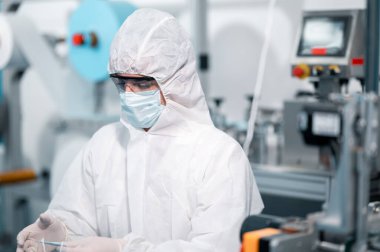 Koruyucu giysi giyen bilim adamları, endüstriyel bir fabrikanın laboratuarında maske yapan bilim adamları. Anti-virüs üretim deposu. Güvenlik ve önleme konsepti Coronavirus covid-19.