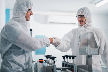 Üniforma giyen iki bilim adamı. Üretim sürecinin yüz maskelerini kontrol et. Endüstri tesislerindeki bir laboratuvarda makinelerle. Güvenlik ve koruma konsepti Coronavirus covid-19.