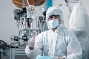 Bilim adamları üniforma giyiyorlar. Yüz maskelerinin üretim sürecini kontrol et. Sanayi tesislerindeki bir laboratuvarda. Güvenlik ve koruma konsepti Coronavirus covid-19.