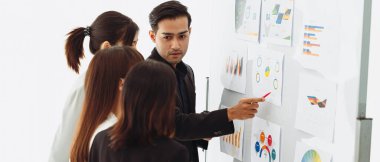 İş adamı veya yönetici bir tartışma grafiği ve stratejik bir planlama raporu sunarak atölyedeki meslektaşlarıyla kârları artırmanın yollarını tartışıyor. Beyin fırtınası ve takım çalışması konsepti.