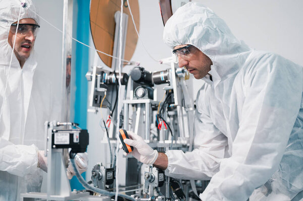 Two scientists wearing uniform protection. Check the manufacturing process face masks. With machinery in a laboratory at industry plants. The concept for security and protection coronavirus covid-19.