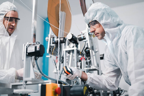 Two scientists wearing uniform protection. Check the manufacturing process face masks. With machinery in a laboratory at industry plants. The concept for security and protection coronavirus covid-19.