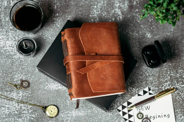 Notebook in a brown leather cover on a black background office style stationery pen clock