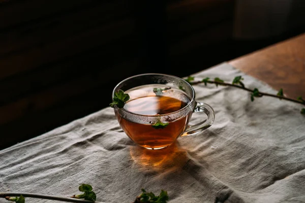 Keten çay örtüsünün üzerinde üzümlü çay ve cam fincanda frenk üzümü.