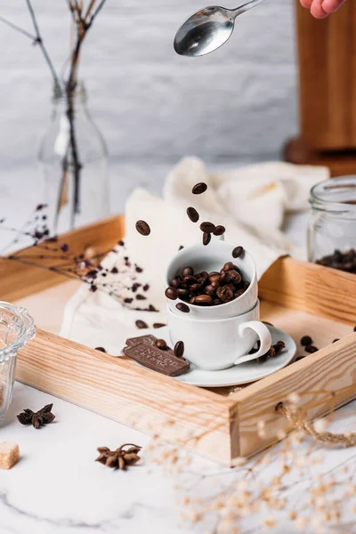 Cocoa beans in a white coffee cup on a wooden tray are poured from a spoon freezing motion