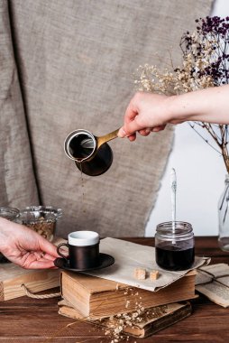 Bir el, çakmaktaşından kahveyi bir kitabın yanında duran bakır bardağa döküyor.