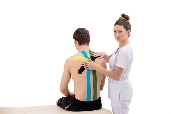 Fisioterapista femminile che mette il nastro di cinesiologia sui pazienti indietro isolati su bianco — Foto Stock