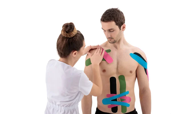 Fisioterapeuta femenina colocando cinta de cinesiología en el hombro de las pacientes aisladas en blanco —  Fotos de Stock