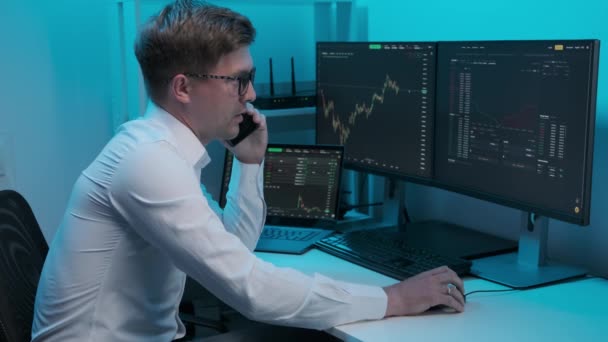Az irodában dolgozó, számítógépekkel teli pénzügyi kereskedő telefonon beszél, amikor a pénzügyi világpiacon kereskedik. — Stock videók