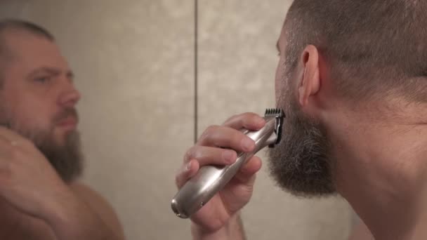 Mężczyzna gładko goli ściernisko maszyną do golenia. Przystojny mężczyzna w średnim wieku goli policzek elektryczną maszynką do golenia.. — Wideo stockowe