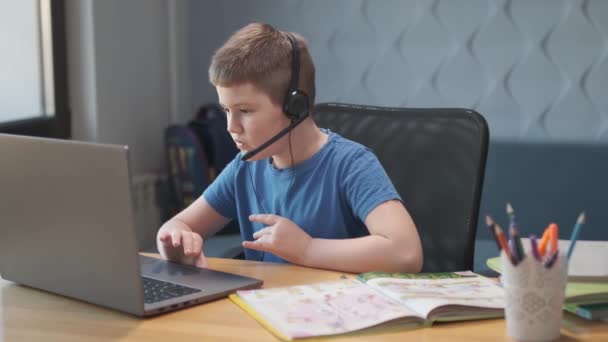 Дистанционное обучение, мальчик-подросток сидит на столе в гостиной и использует ноутбук для изучения в самоизоляции дома, домашнее обучение онлайн по видеокассетам — стоковое видео