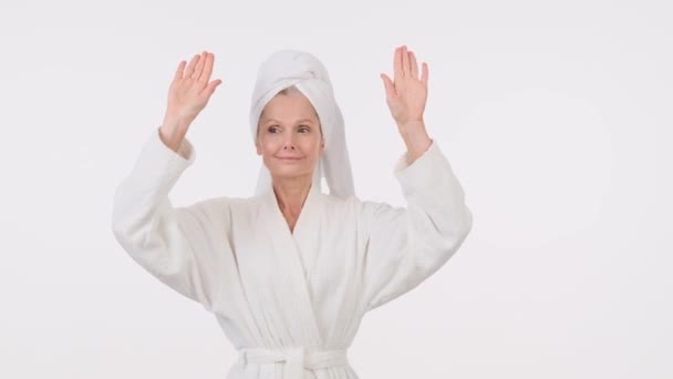 一位漂亮的老年妇女 身穿浴衣 头上披着毛巾 双手捂着白底 — 图库视频影像